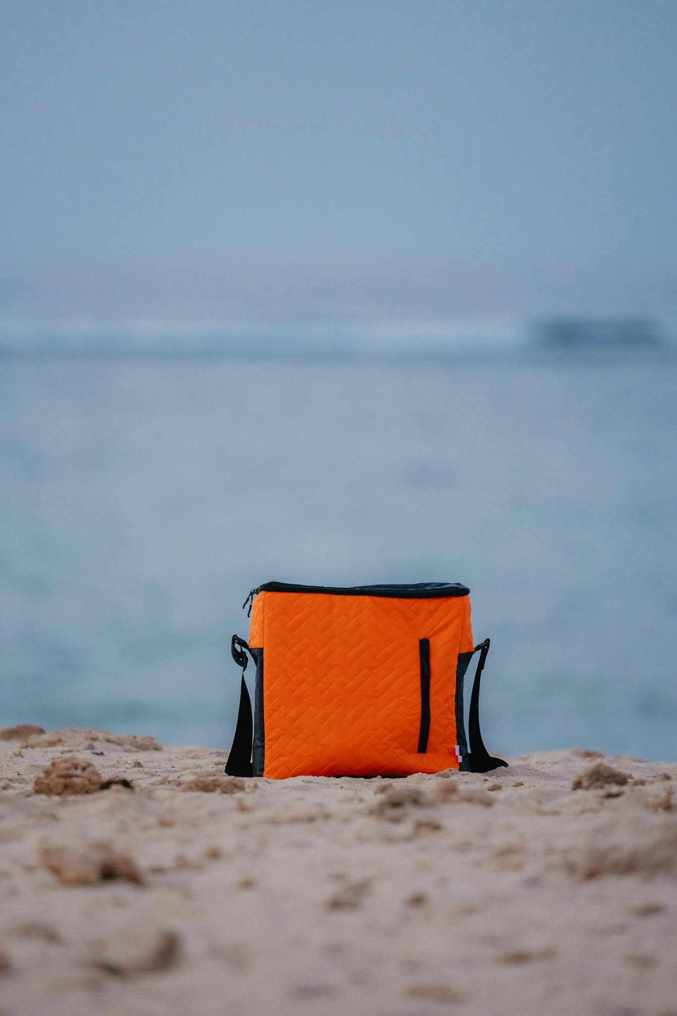 Bright orange cooler bag resting on a sandy beach in Marsa Alam, Egypt, by the Red Sea shore.